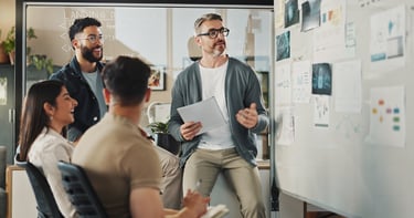 An employee reviews a report with his colleagues in front of a whiteboard.