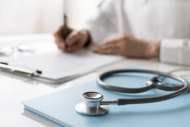 A doctor writes a report while a stethoscope lays on top of a patient file. 