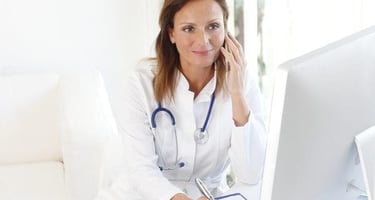 A female nurse wearing a stethoscope takes a call on a cellphone while in a medical office. 