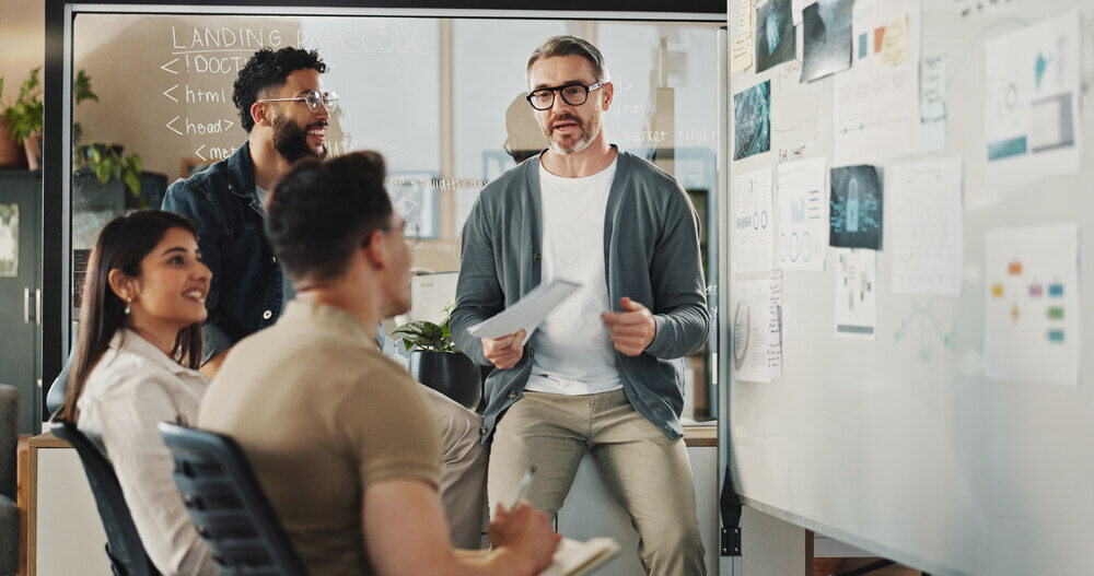 An employee reviews a report with his colleagues in front of a whiteboard.