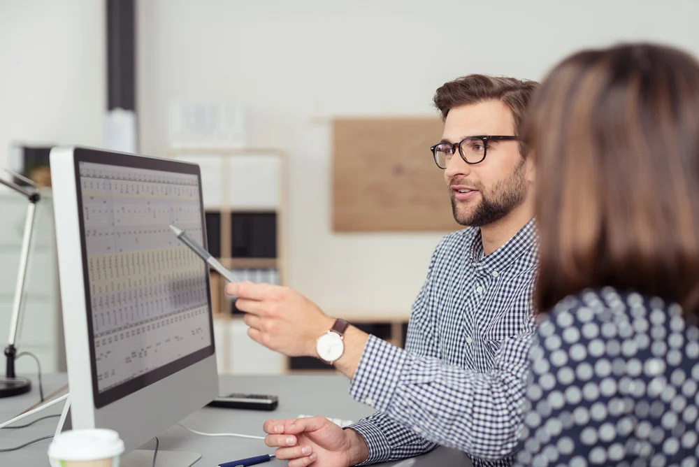 Male employee explaining something on a computer screen to a female employee.